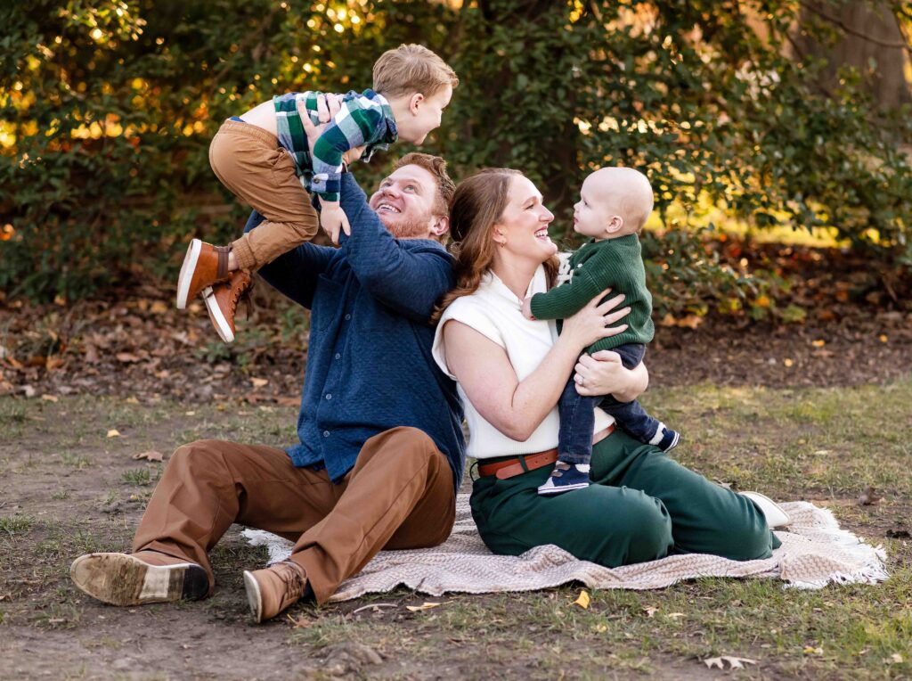 A family of four plays with their small sons in an outdoor family photo session in St. Louis, Missouri.