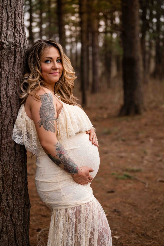"Stylish outdoor maternity portrait at Busch Conservation Area featuring pregnant woman in lace dress with tattoos, cradling baby bump during golden hour — inspiration for bold and natural pregnancy photography."