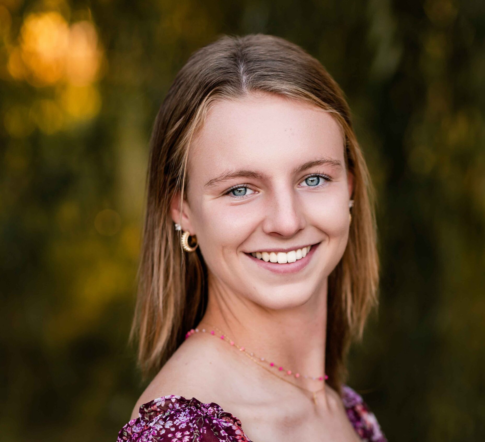 Senior girl smiling in a maroon floral dress with greenery in the background at Tower Grove Park, St. Louis.
