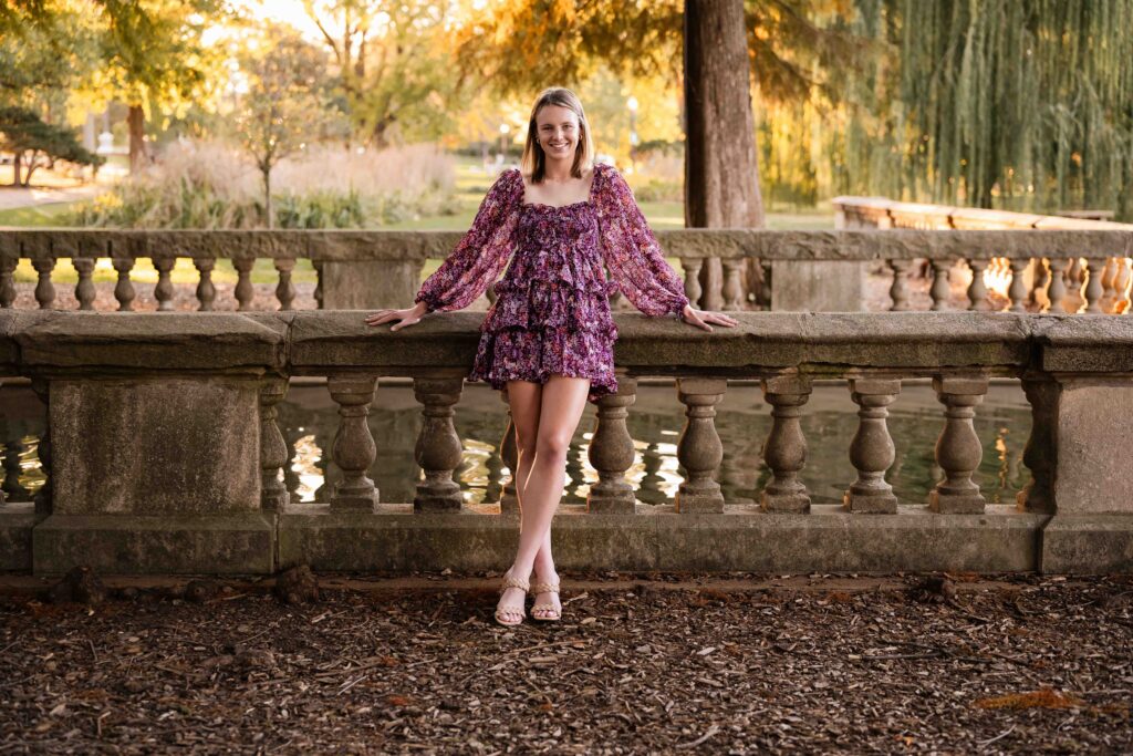 Senior girl sitting on a stone railing overlooking autumn trees at Tower Grove Park in St. Louis.