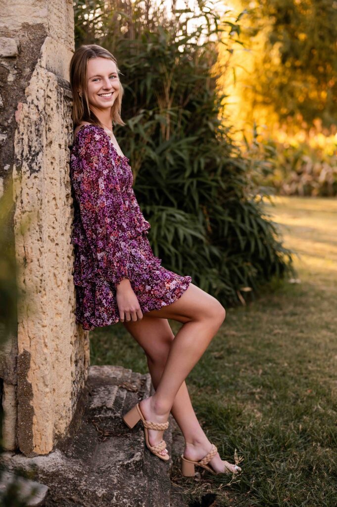 Teen girl in a maroon patterned dress leaning against a stone column at the Ruins at Tower Grove Park during golden hour.