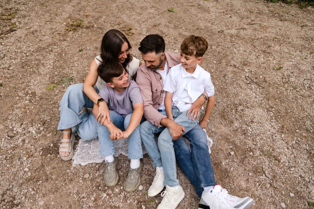 Family of four sitting close together on a gravel trail, enjoying a candid and connected moment during their St. Louis family photo session.