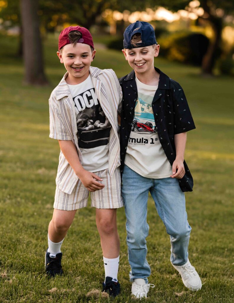 Two brothers playing and laughing in a grassy field at Laumeier Sculpture Park during a playful St. Louis sibling photo session.