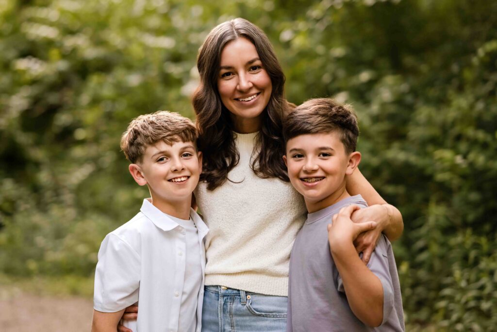 Mother hugging her two sons while standing in front of lush greenery at Laumeier Sculpture Park during golden hour in St. Louis.