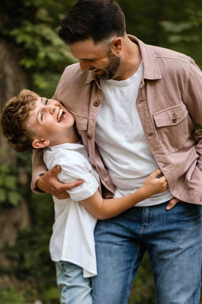 Father and son laughing together under the trees during a light-hearted family photography session in St. Louis, Missouri.