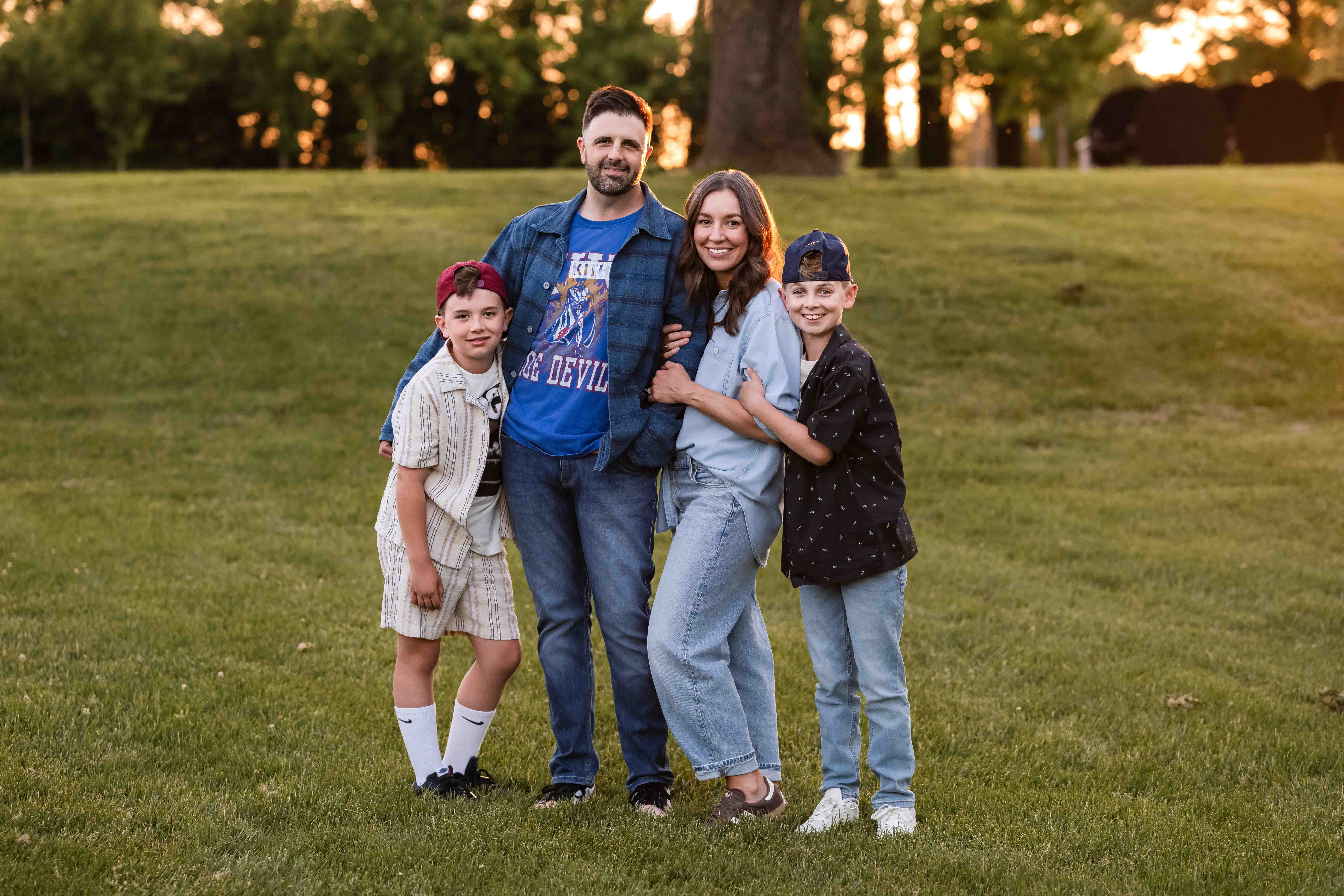 Family of four standing together in a glowing field at Laumeier Sculpture Park, enjoying golden hour during their St. Louis family photo session.