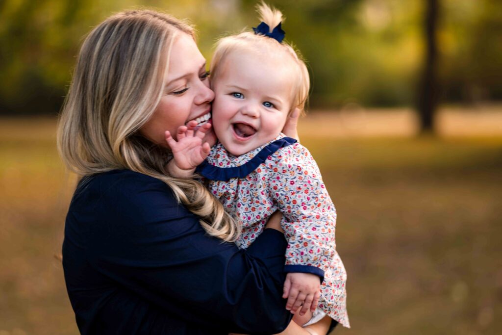 Mom holding her toddler close while both smile warmly in soft golden fall light.