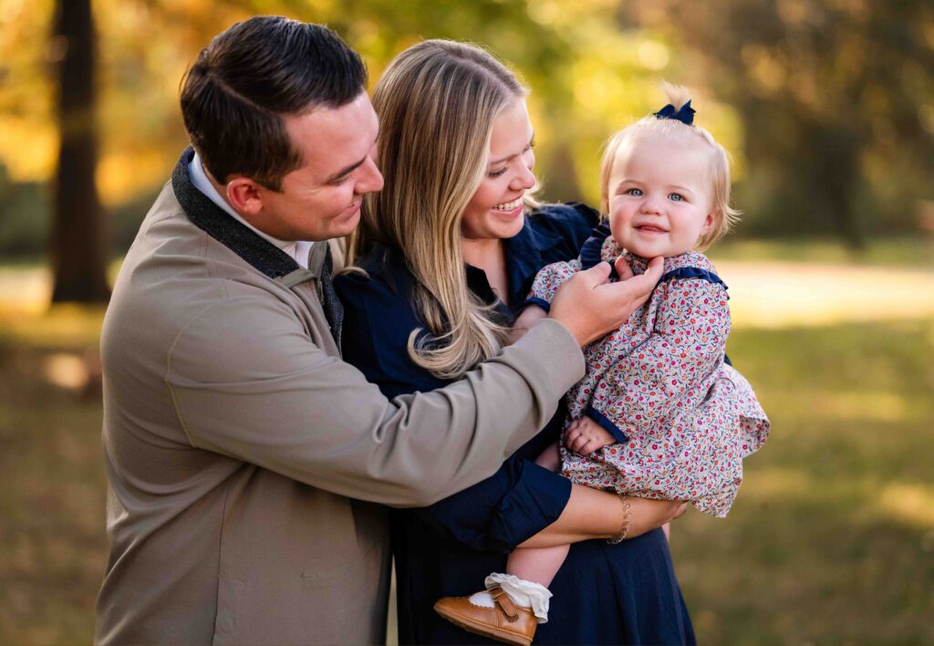 Parents cuddling their toddler between them, laughing together during a fall family photoshoot in St Louis, MO.