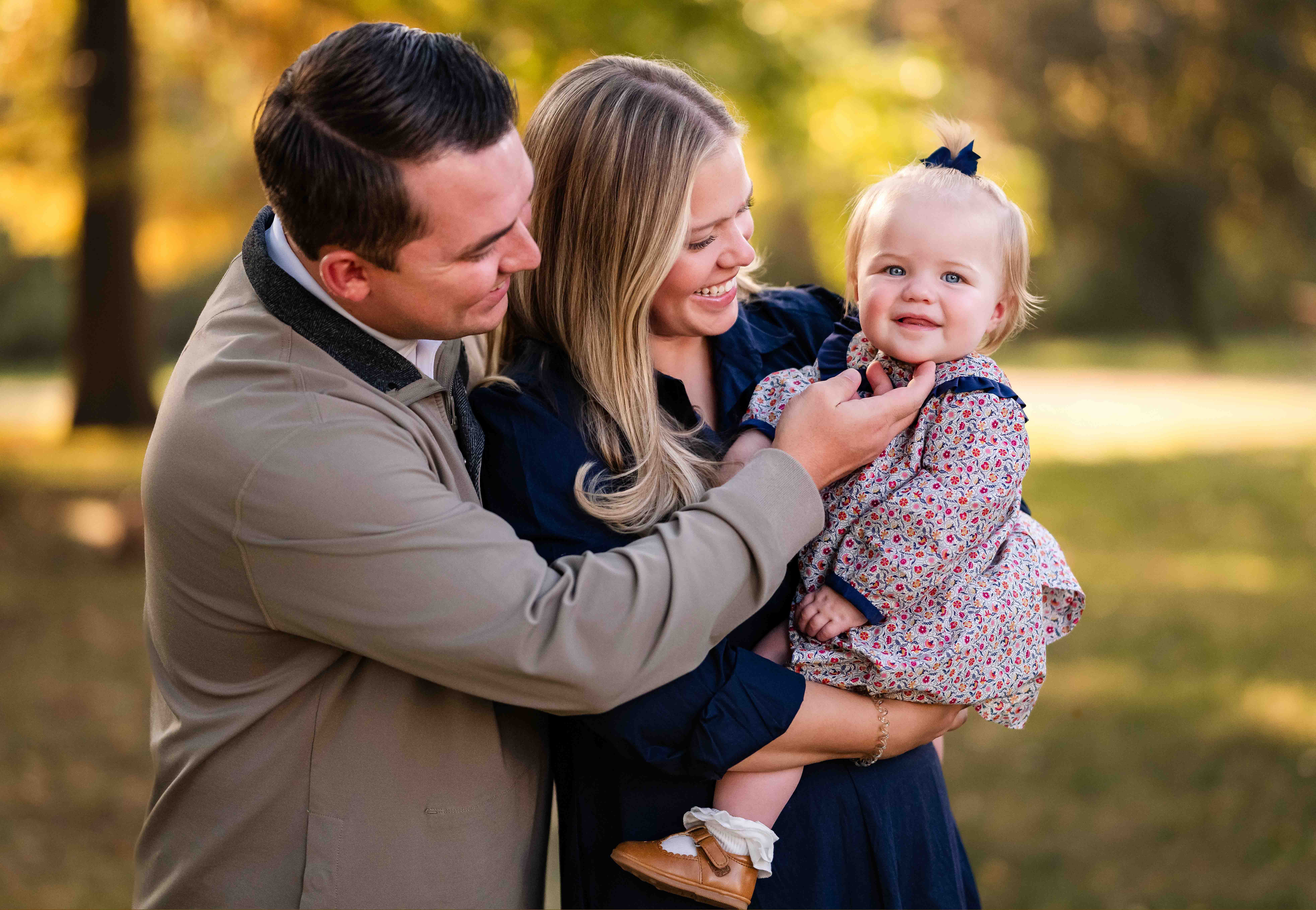 Parents cuddling their toddler between them, laughing together during a fall family photoshoot in St Louis, MO.