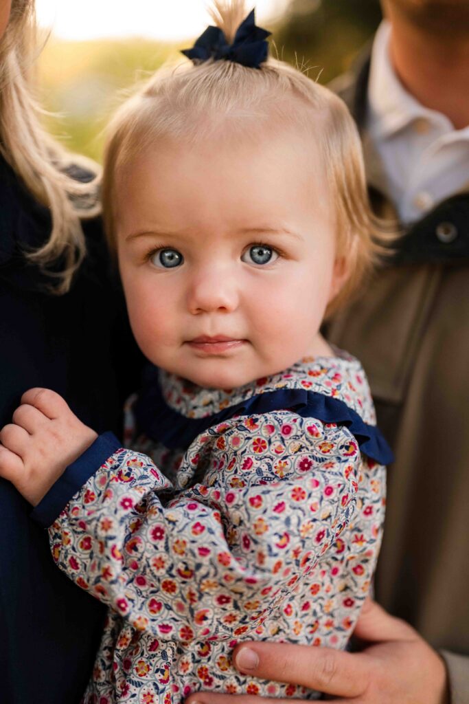Close-up portrait of a toddler with a bow in her hair, looking at the camera during a fall family session in Clayton, MO